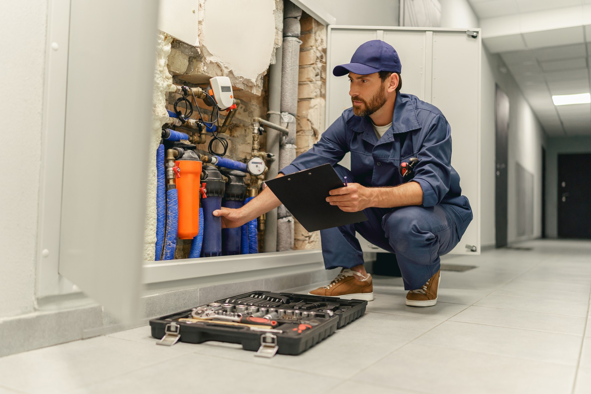 Male plumber diagnoses pipes in water supply system before repairing and makes notes in clipboard